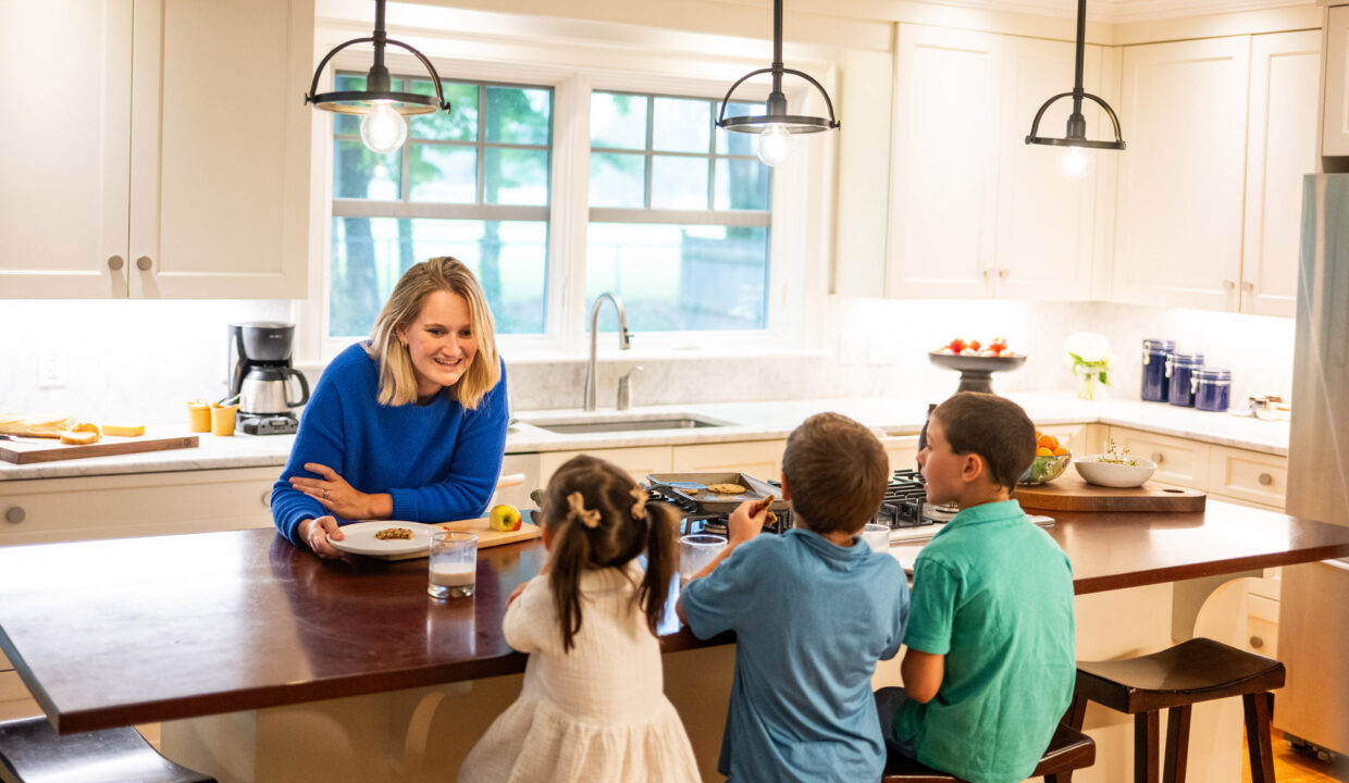 Family gathered at a kitchen island in a bright, well-designed home, reflecting everyday living and the shift toward comfortable, functional spaces that support modern lifestyles